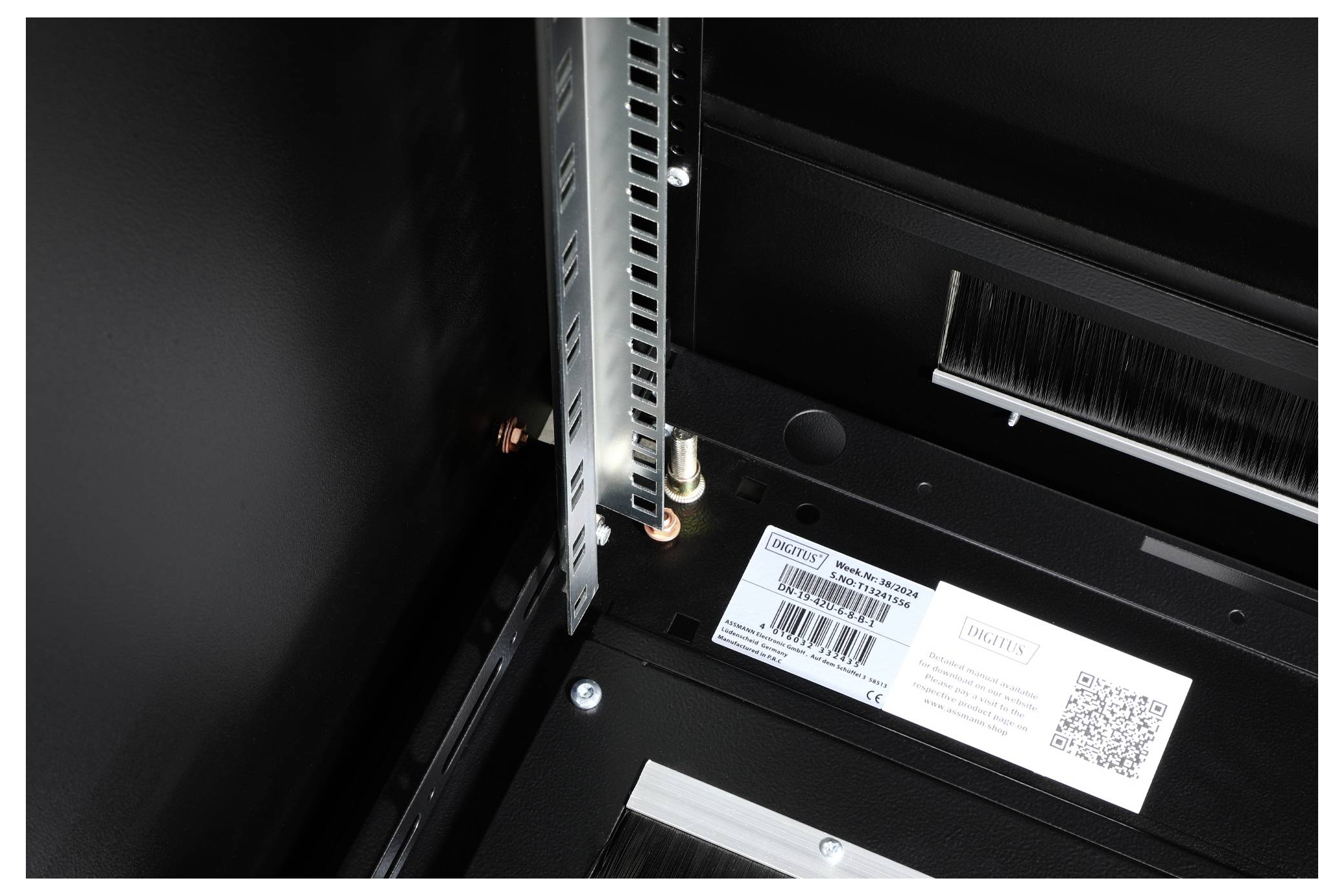 Internal view of a technical device showing visible wiring and a QR code label. A metal frame is visible in the top left corner.