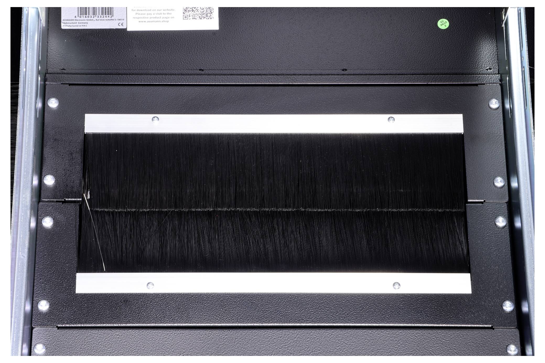 The image depicts a black brush strip mounted in a rectangular metal frame, serving as a protective or guiding element within a device.