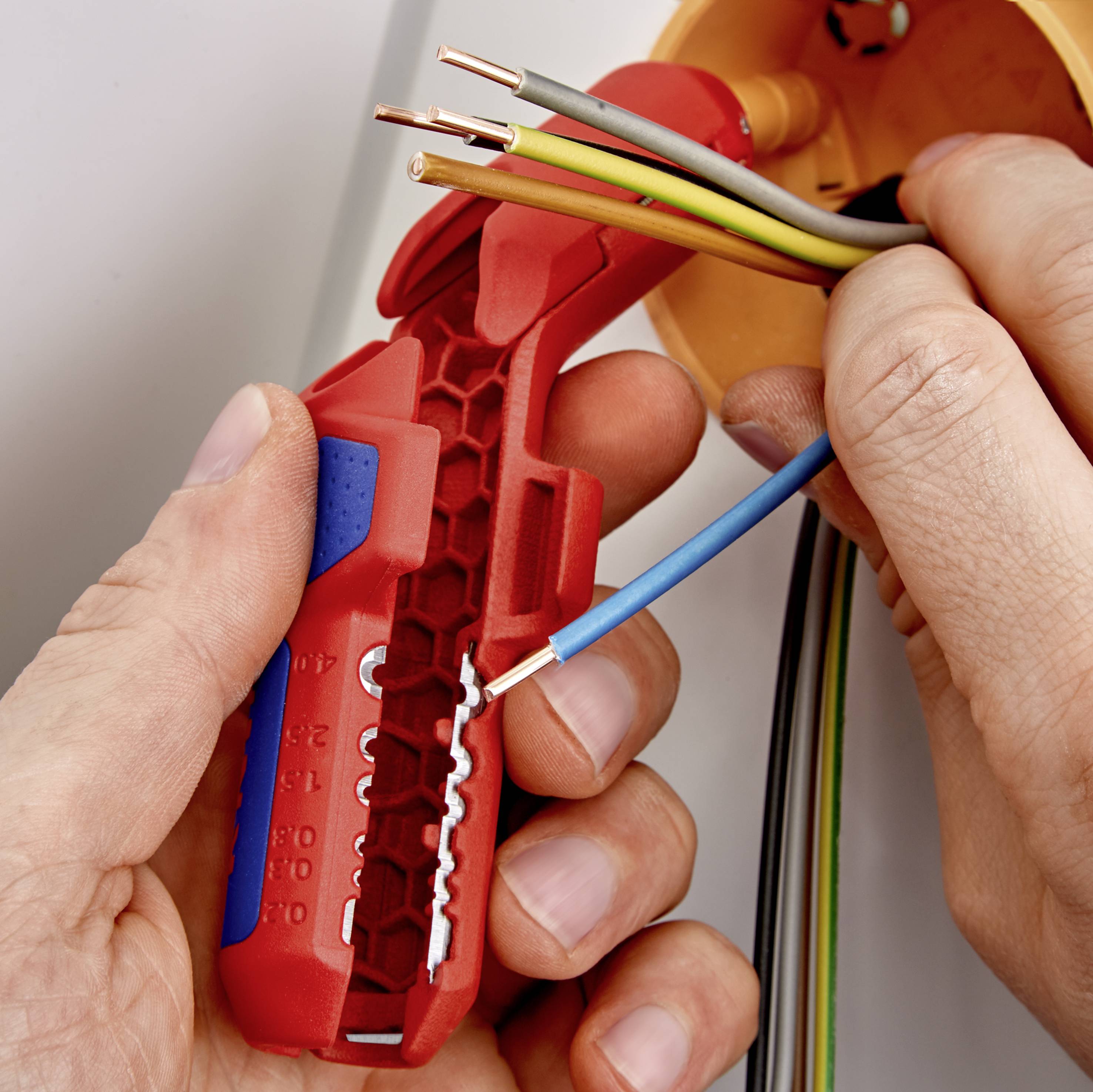 A person is using a wire stripper to remove the insulation from wires. The wires are different colours and partially insulated.