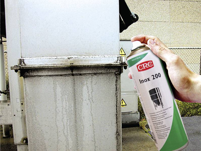 A hand is holding a spray can 'CRC Inox 200' in front of a metallic surface. Product for the care and protection of stainless steel.