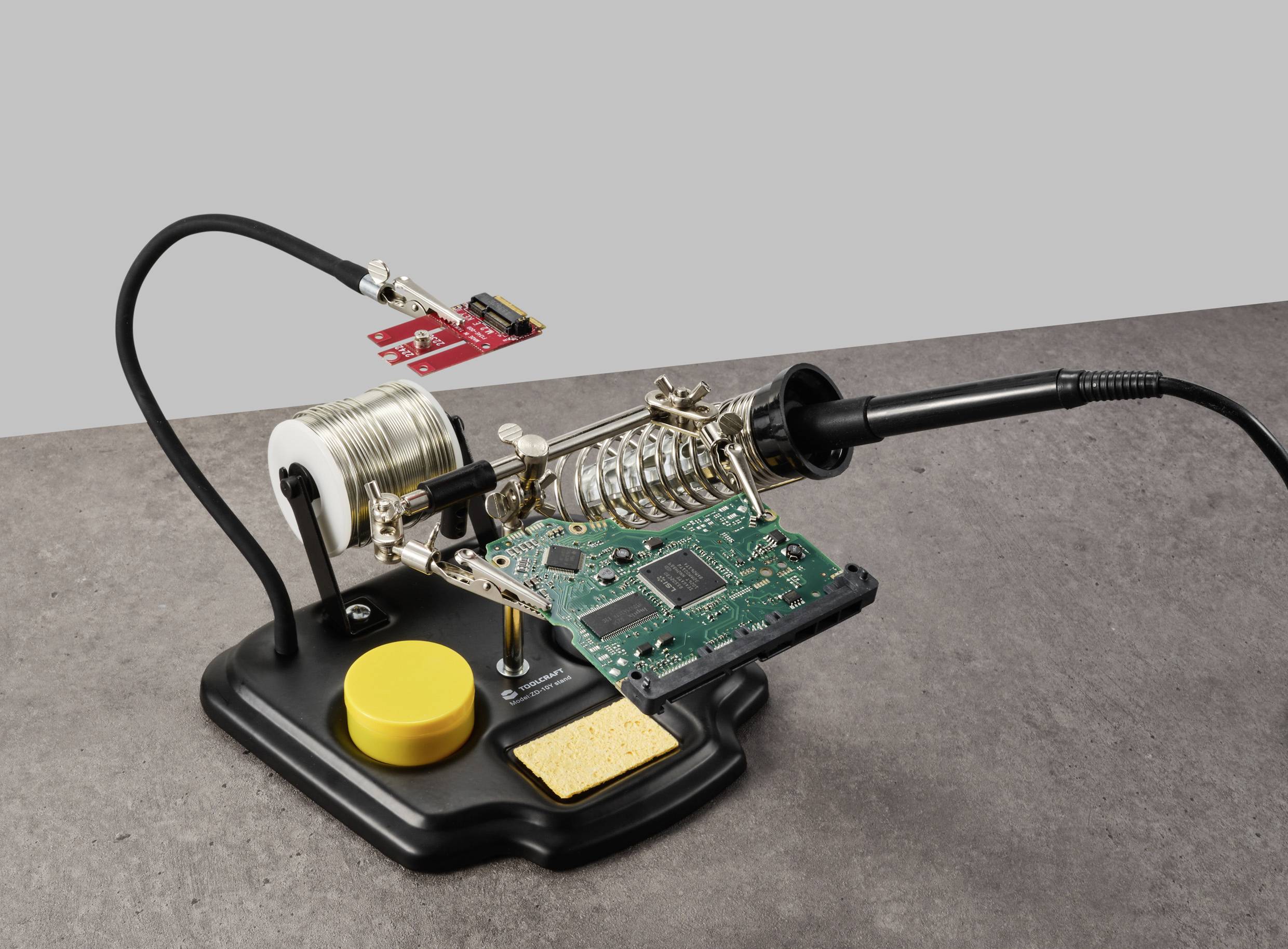 Electronics workbench with soldering iron, circuit board, solder wire, holder and cleaning block, symbolising electronics repair.