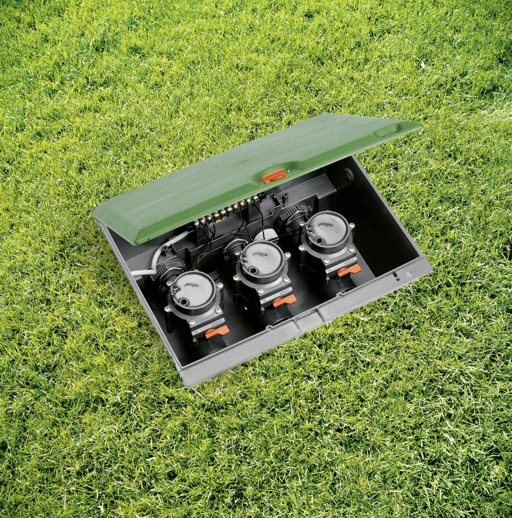 A green plastic box with an open lid contains three electrical sockets and is placed on a lawn.