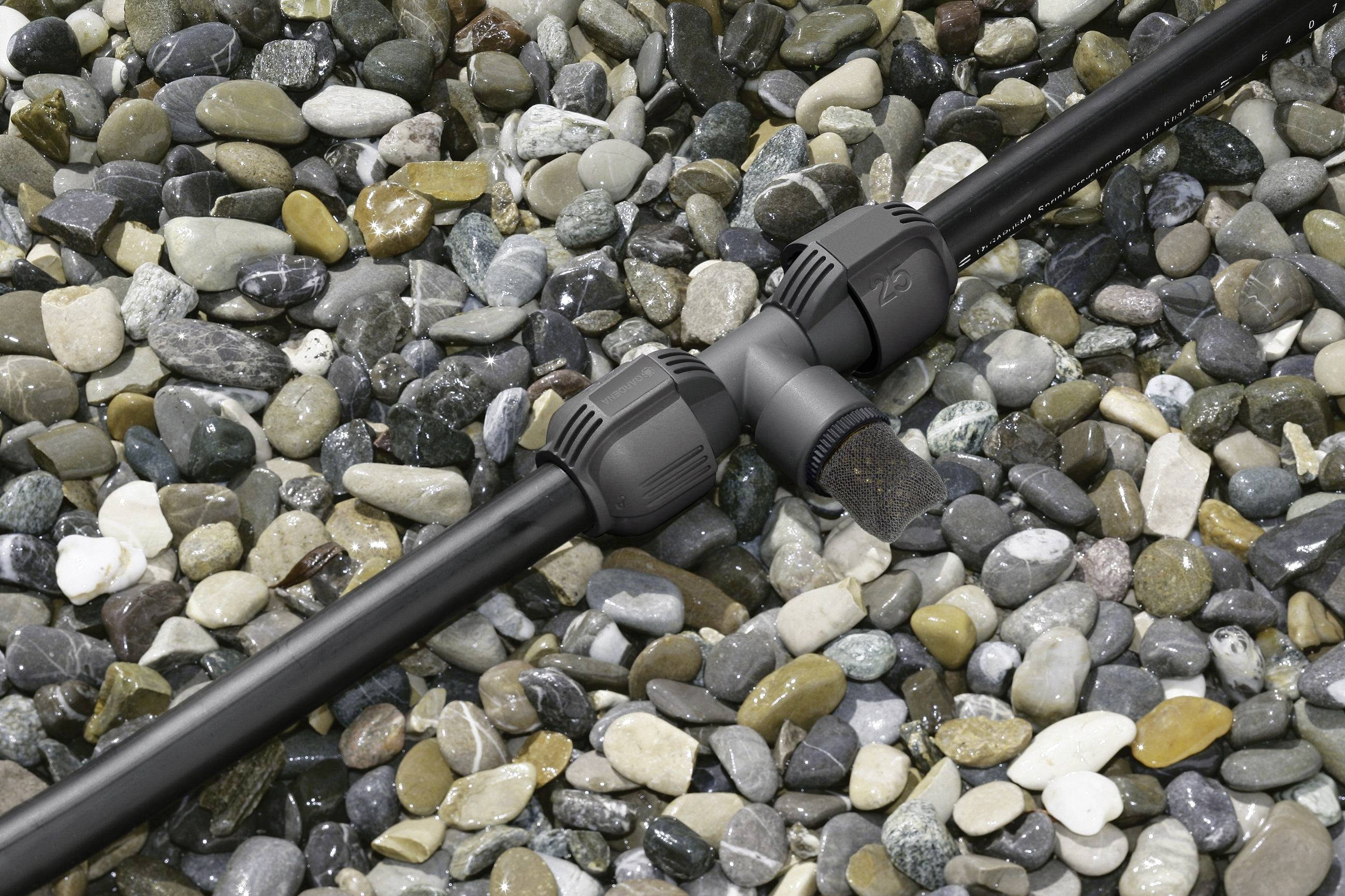 An irrigation pipe with a T-junction on a base of colourful pebbles, ready for garden irrigation systems.