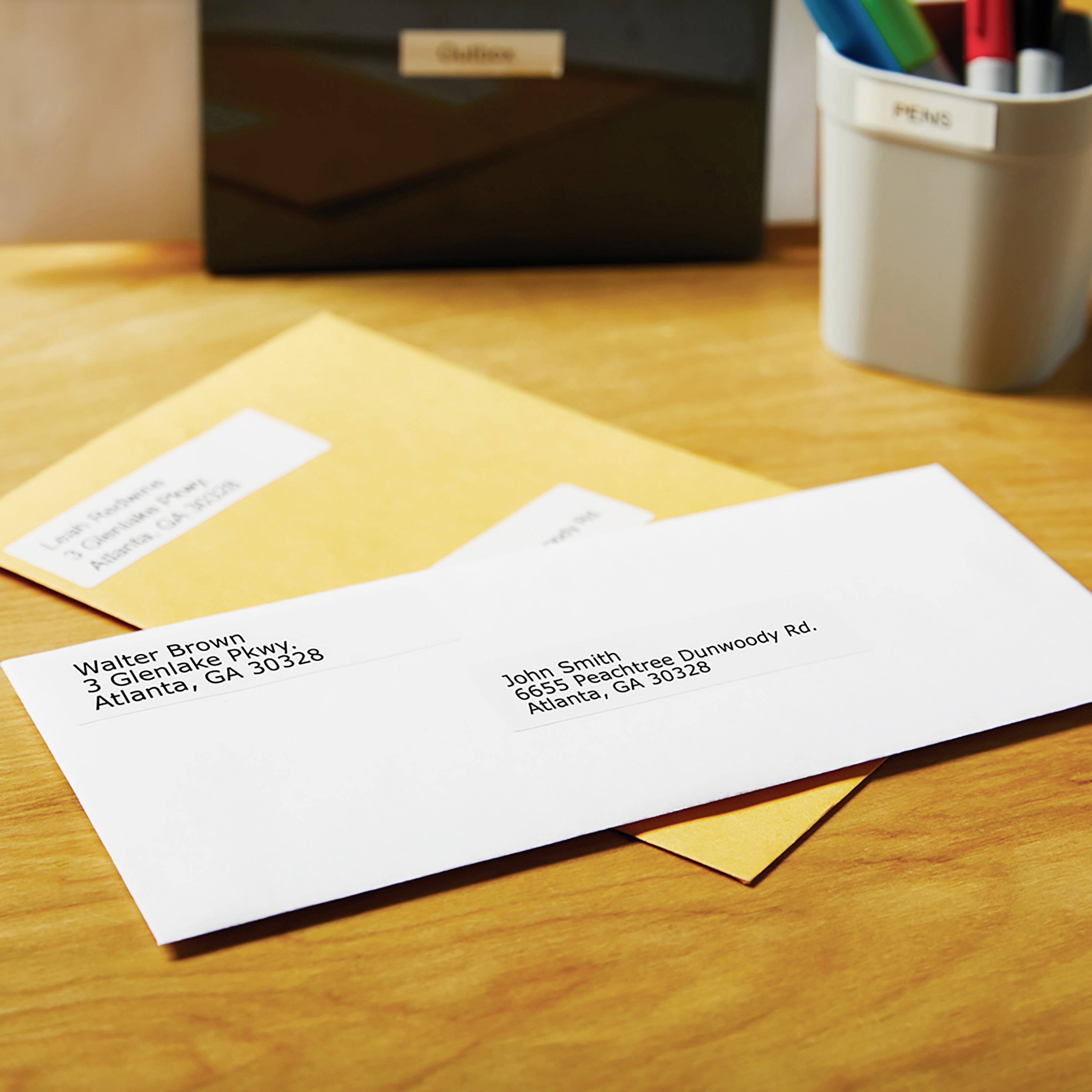 Envelopes and a pen holder on a desk. Address labels display names and addresses in Atlanta, GA.