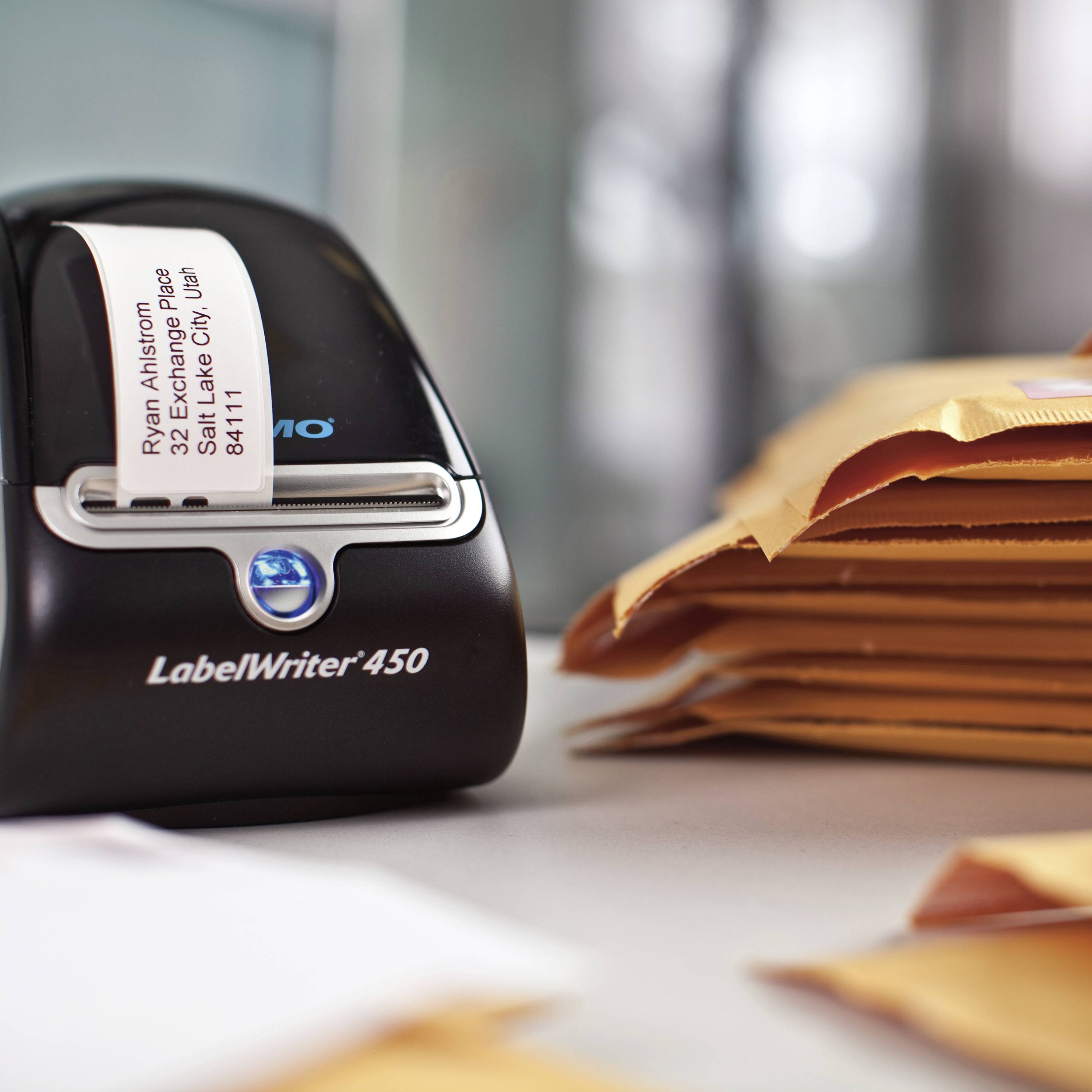 A LabelWriter 450 label printer is printing a label with an address next to a stack of orange envelopes.