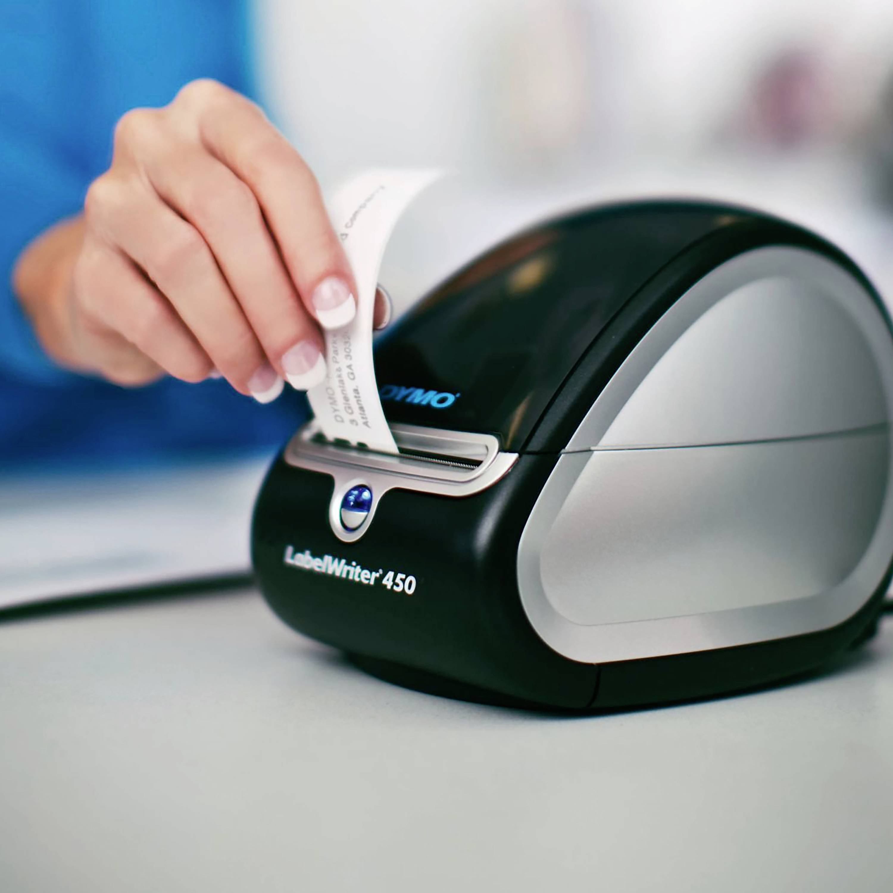 A hand pulls a labelled tag from a compact, black label printer on a table.