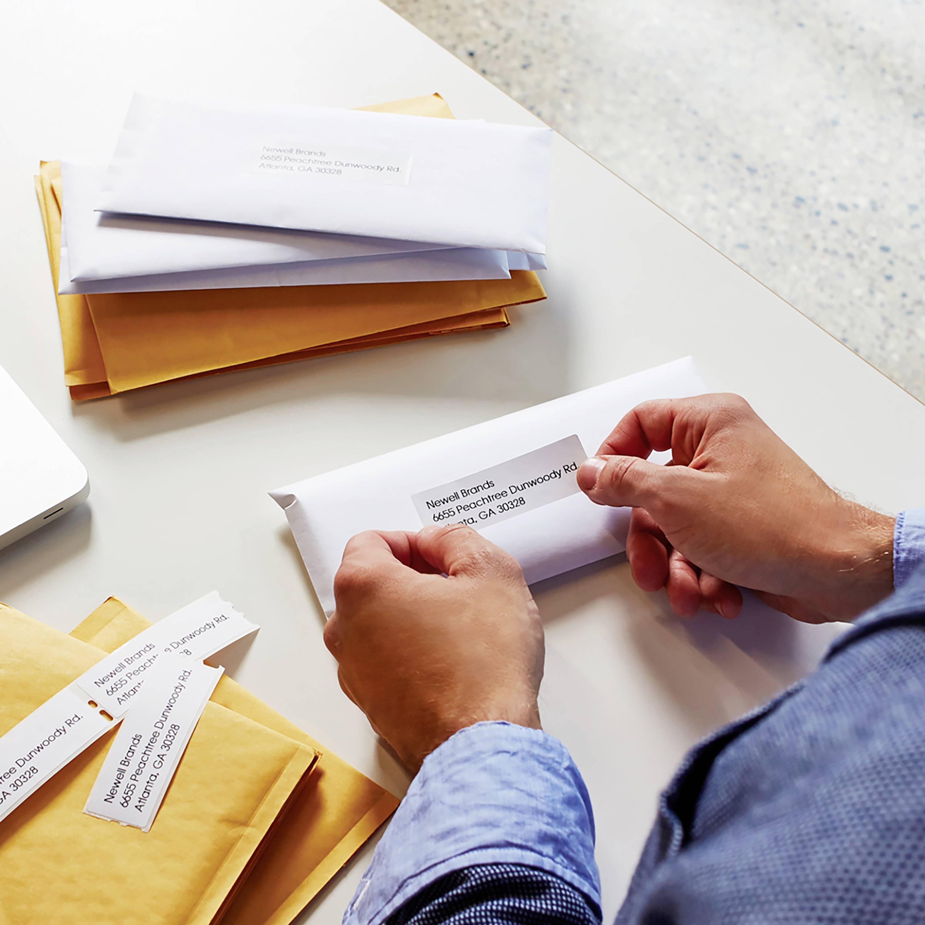 A person wearing a blue shirt is holding a letter with an address, surrounded by other letters and envelopes on a table.