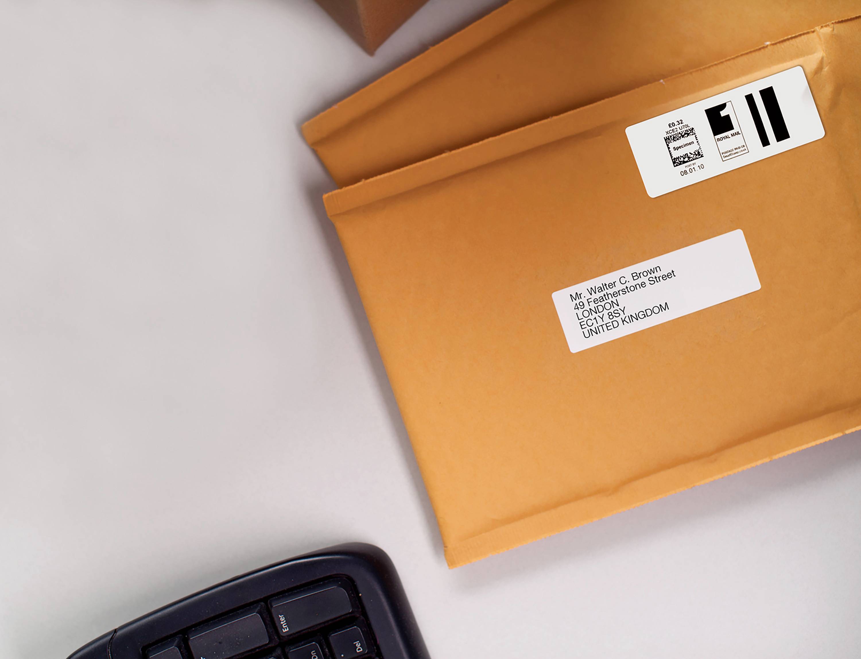 Two orange envelopes with address labels are lying on a desk. Part of a computer keyboard is visible.