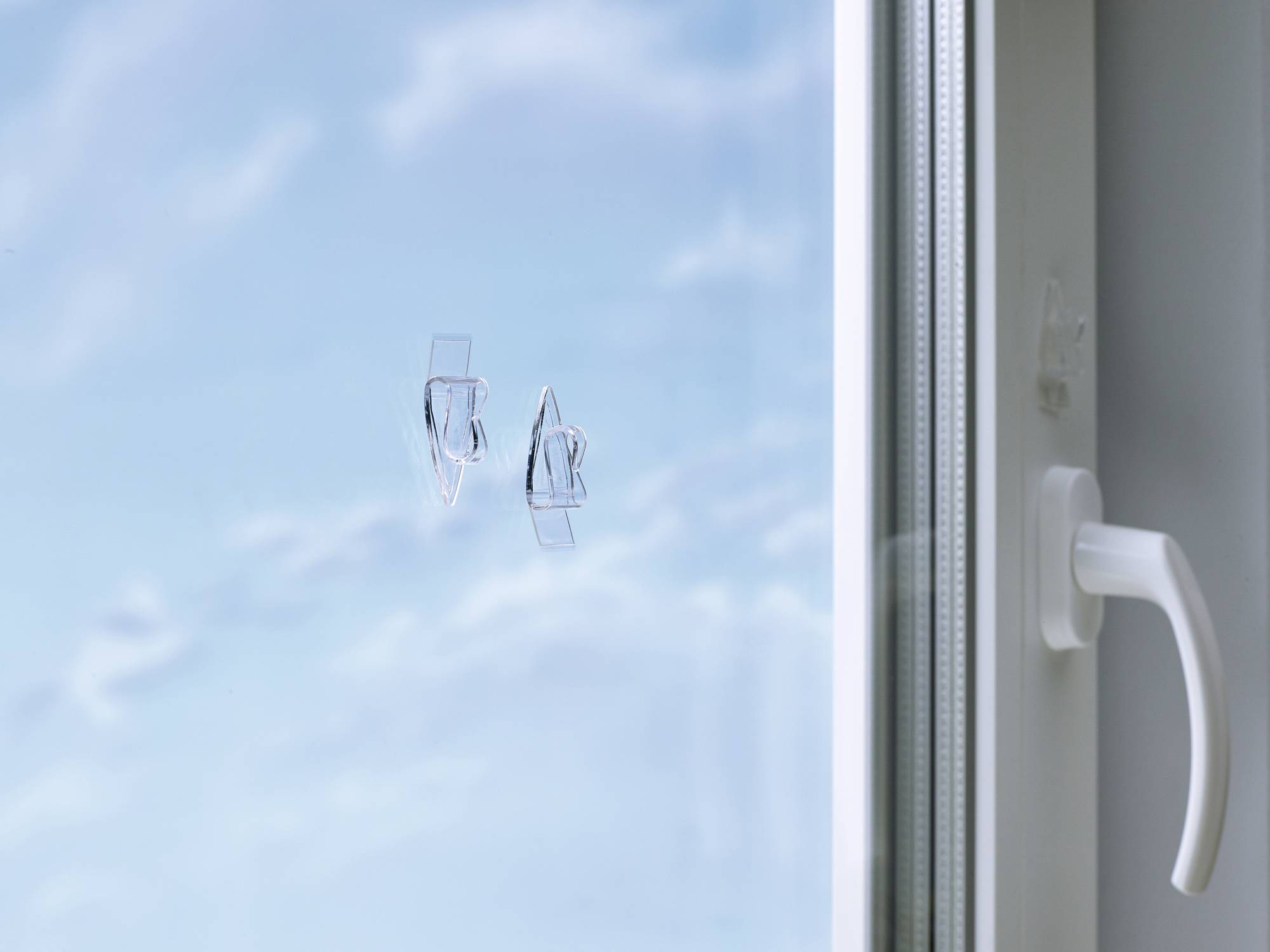 A closed window against a background of blue sky and clouds, with a white window handle on the right side.