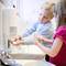 A boy and a girl are washing their hands at a sink, using soap from a dispenser.