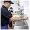 Food-service worker washing hands at an industrial sink in a kitchen, with another worker preparing food in the background.