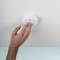 A hand is testing a smoke detector on the ceiling. The detector is round and white, crucial for indoor safety.