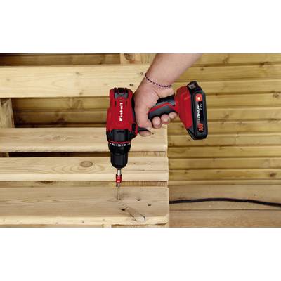 A person is securing a screw in a wooden board with a red cordless drill, with wooden panelling in the background.