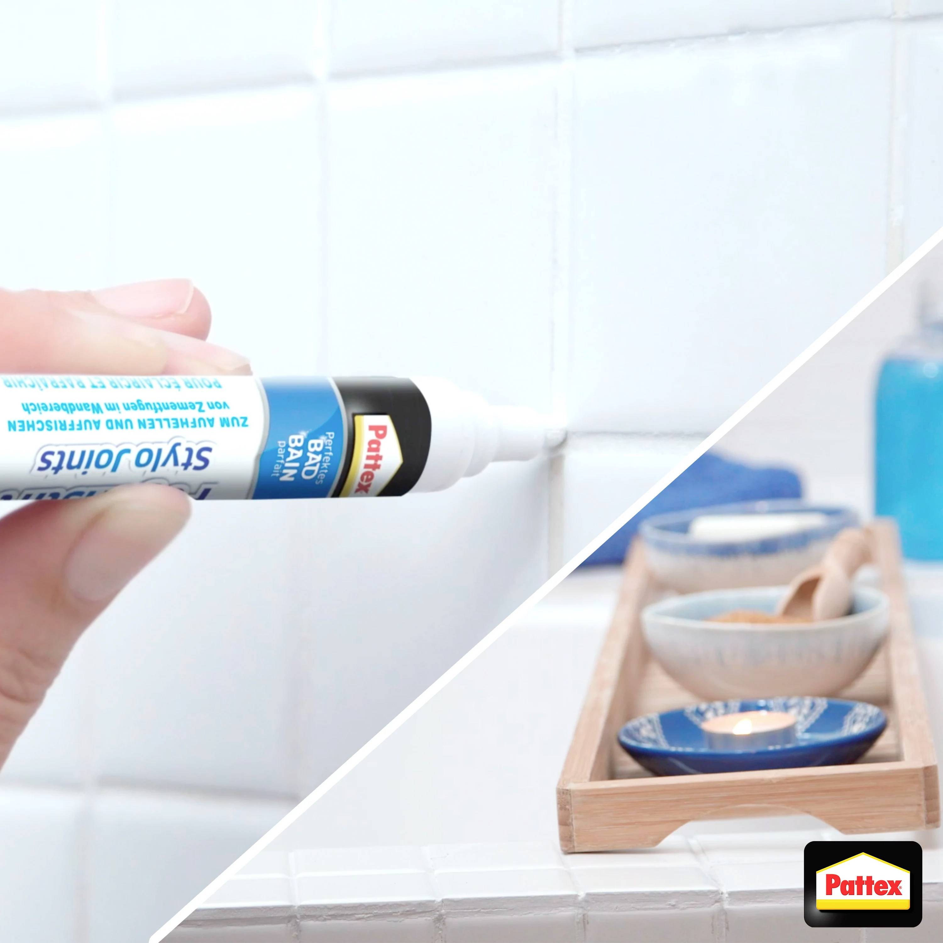 A hand is applying a white grout pen to the joint between white tiles. Blue accessories are visible in the background.