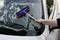 A person is cleaning the windscreen of a car with a blue window squeegee. Soapy water is visible on the glass.