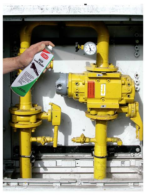 A person holds a can of 'CRC Leak Finder' spray near yellow gas pipes with a pressure gauge, likely checking for gas leaks.