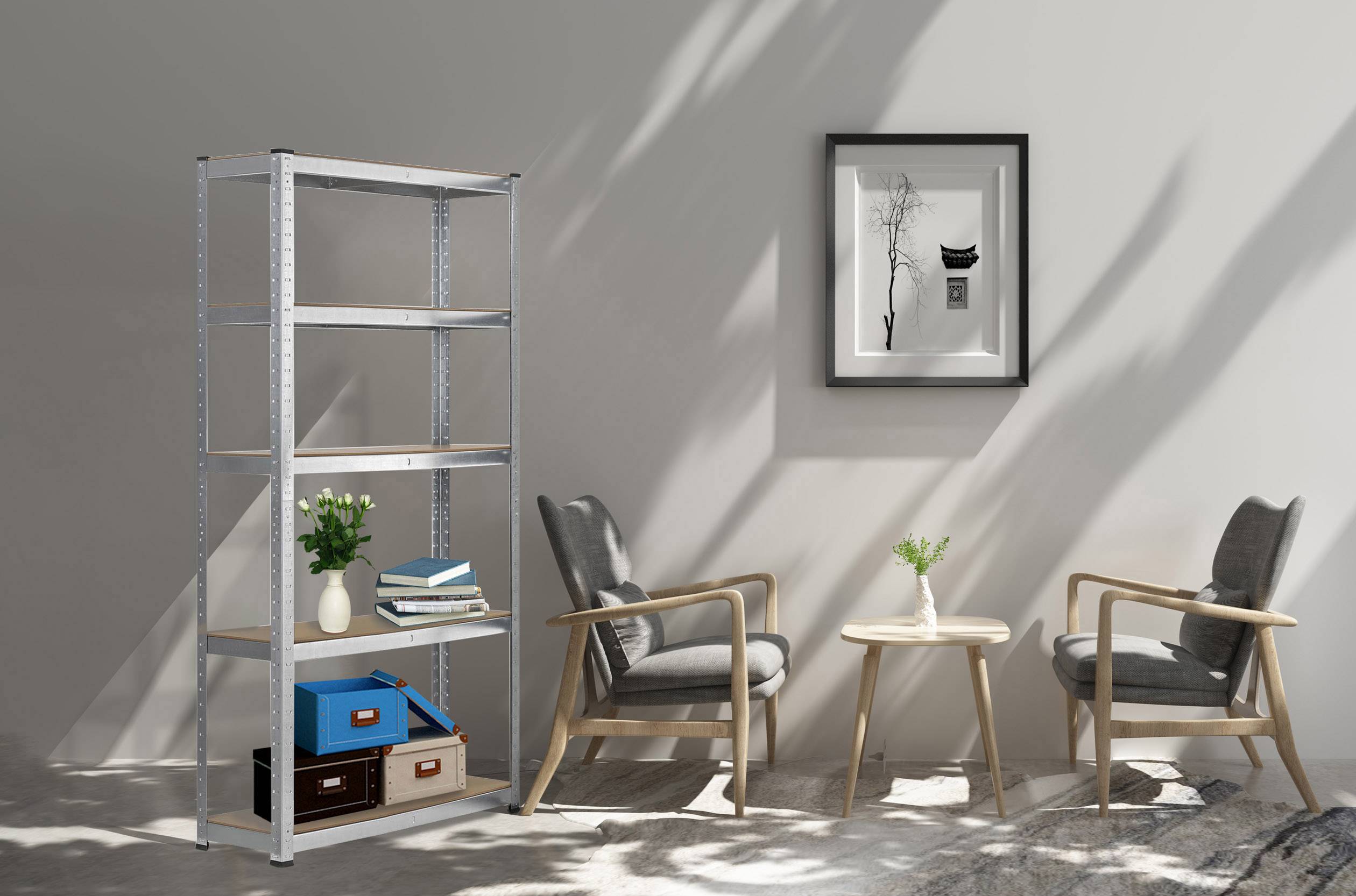 Two grey armchairs around a wooden table with flowers, next to a bookshelf with books and boxes. A black and white picture hangs on the wall.