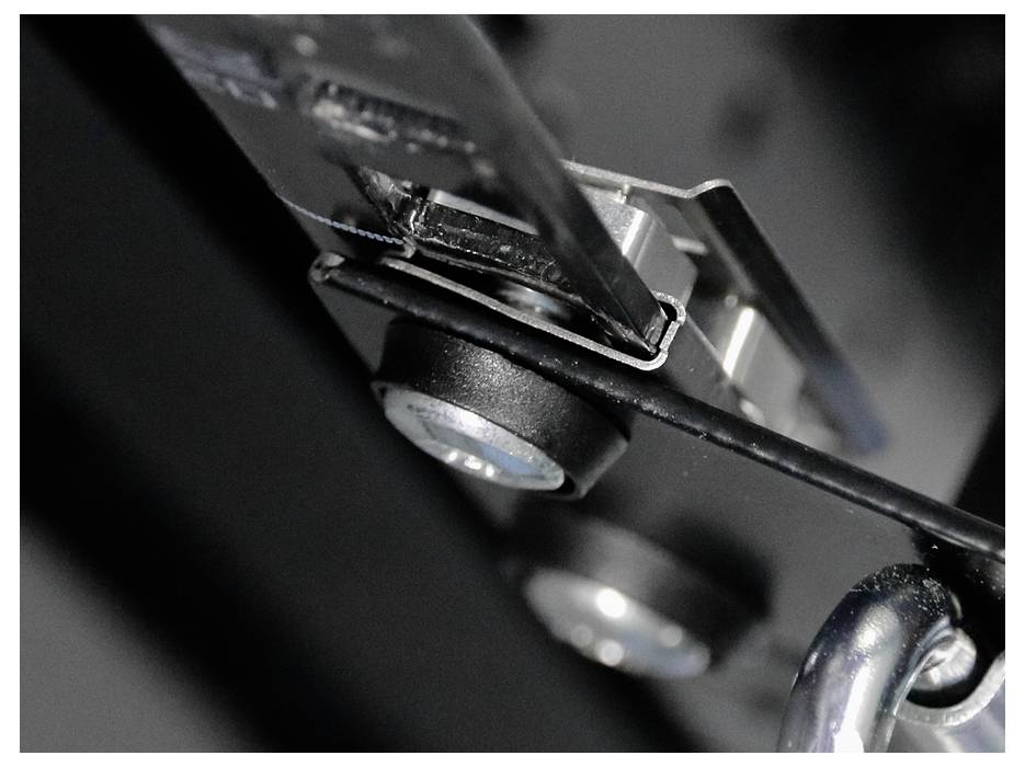 Close-up of a metal mechanism with screws, hinges, and a chain, potentially part of a larger device or machine.