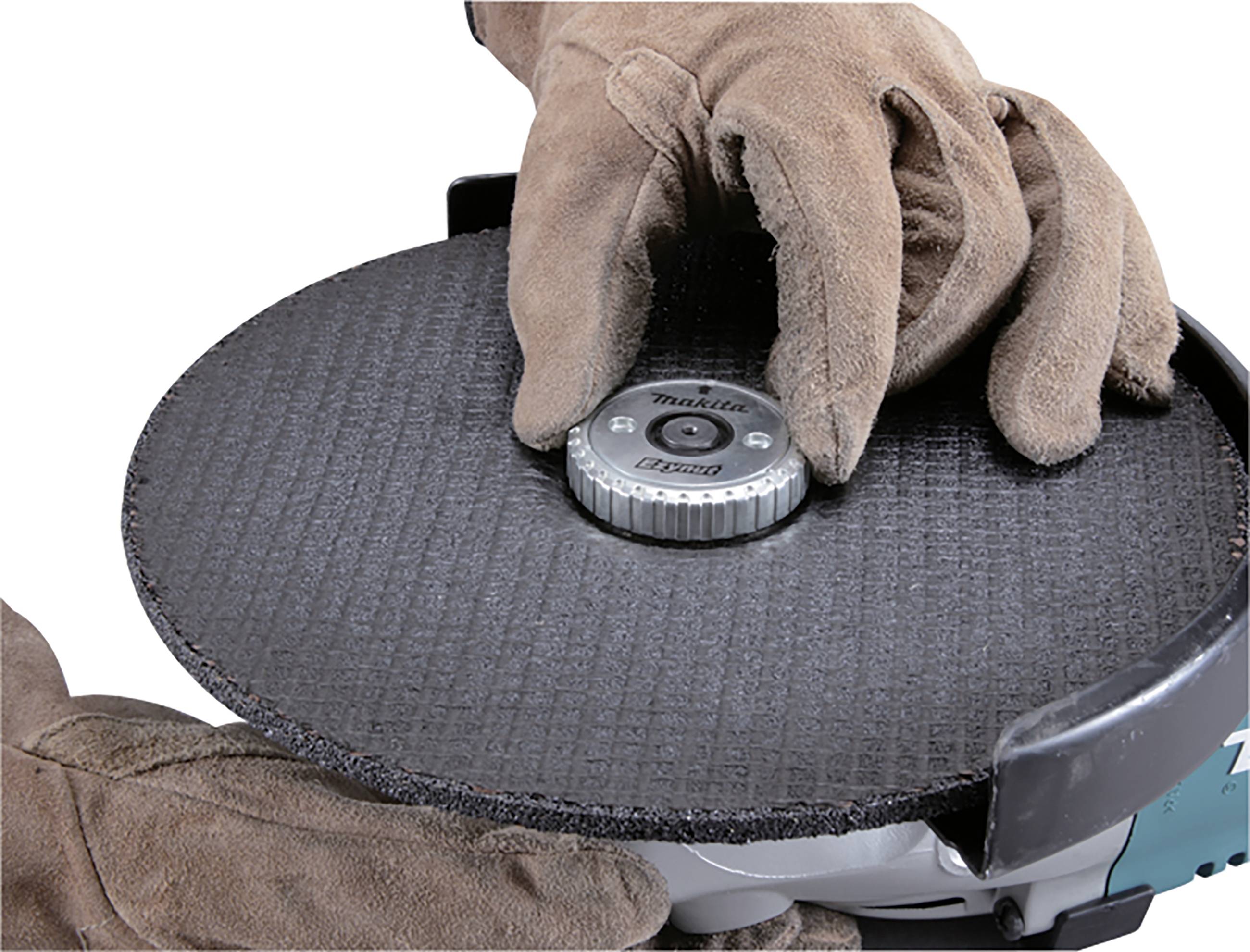 A person wearing gloves is changing the disc of a grinding machine. Focus is on caution and safety when handling the tool.