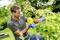 A man is spraying pesticide on leaves in a garden. He is wearing a grey shirt and blue gloves. Rural setting.