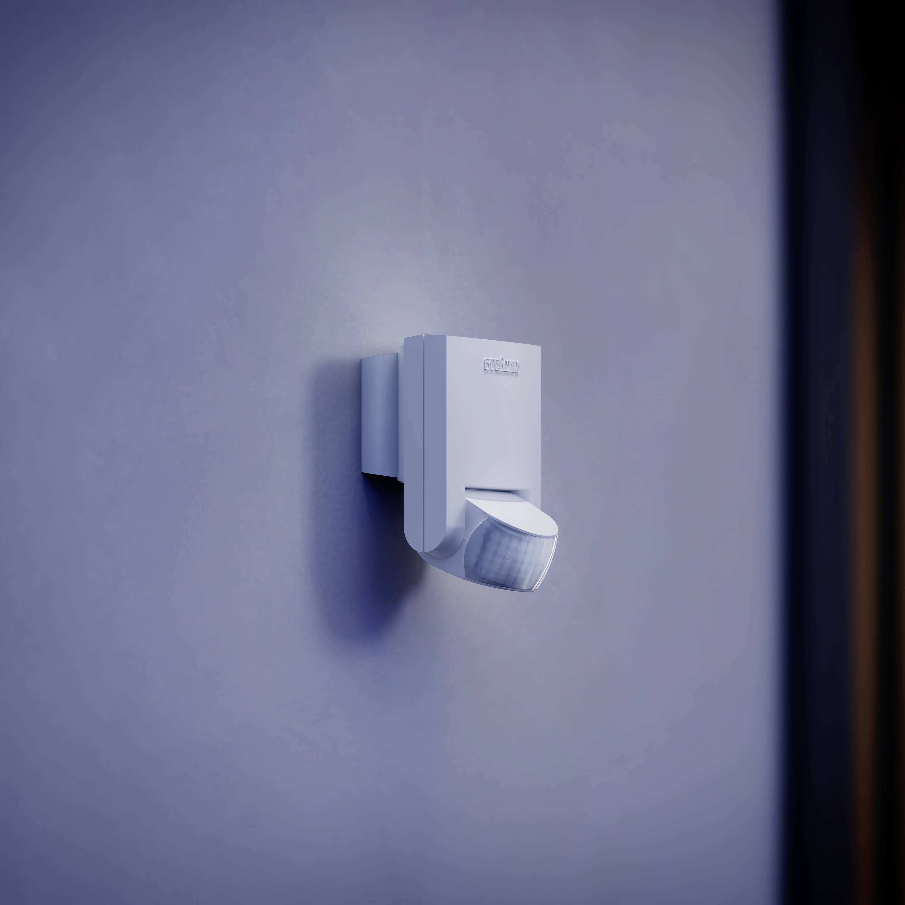 Motion sensor mounted on a blue wall, with a sensor slightly tilted downwards.