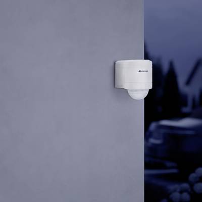 A motion sensor is mounted on a grey wall. A car is blurrily visible in the background.