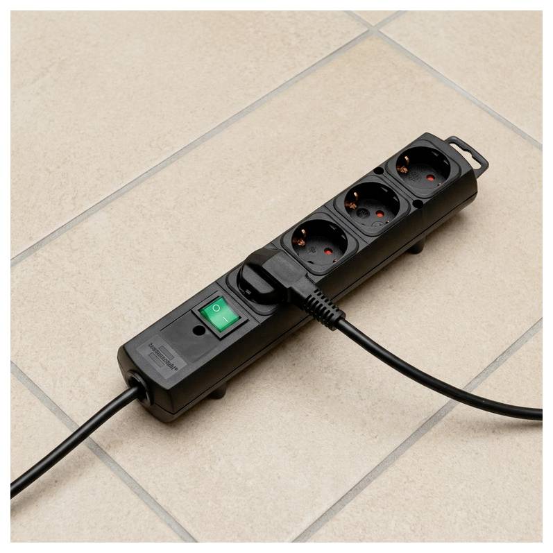 Black power strip with four outlets and green on/off switch on tiled floor, with cords plugged in at both ends.
