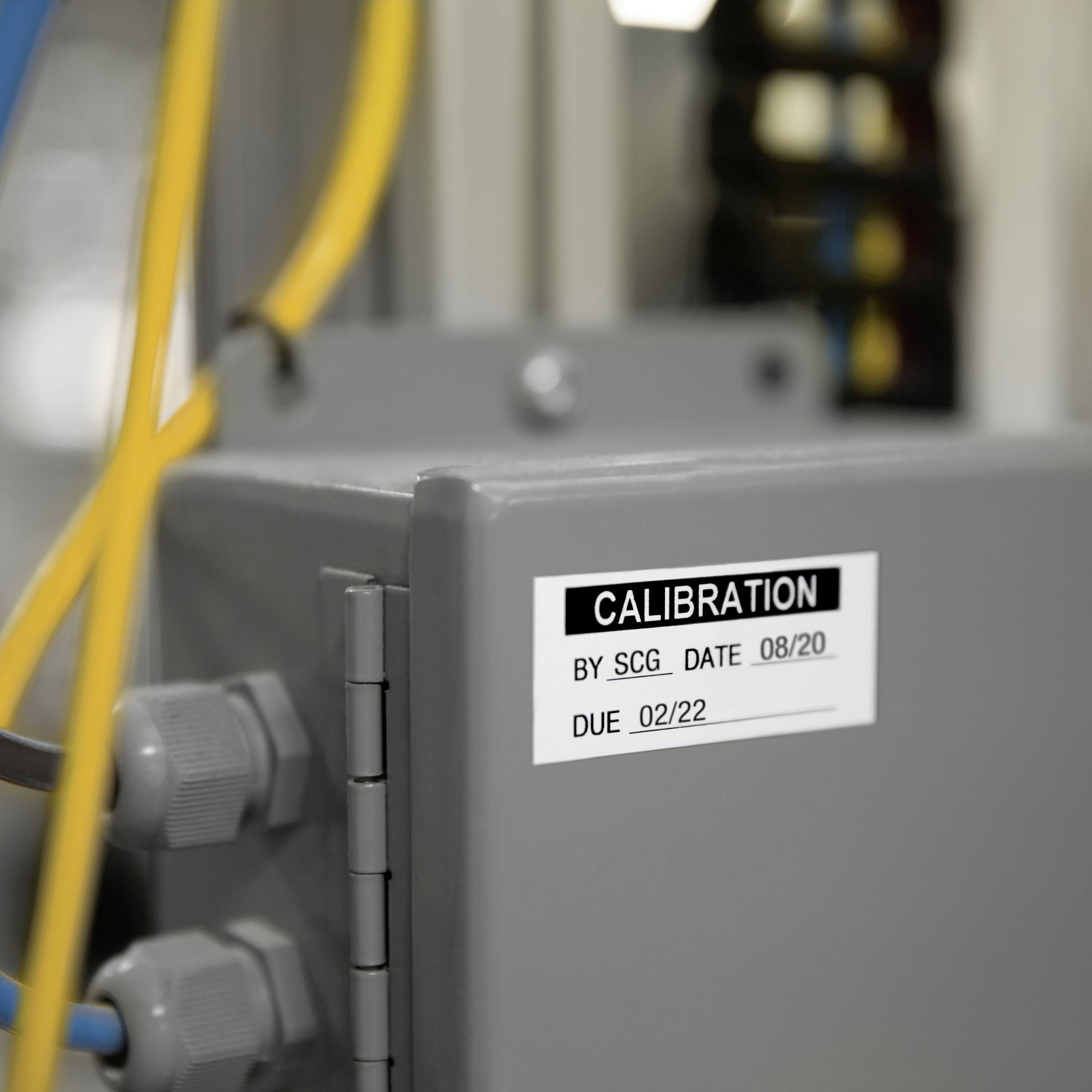 A grey box labelled 'Calibrated by SCG' with the dates '08/20', '02/22', surrounded by cables in the background.