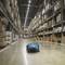 A robot moves autonomously through a large warehouse filled with shelves and packages. The floor is clean and well-lit.