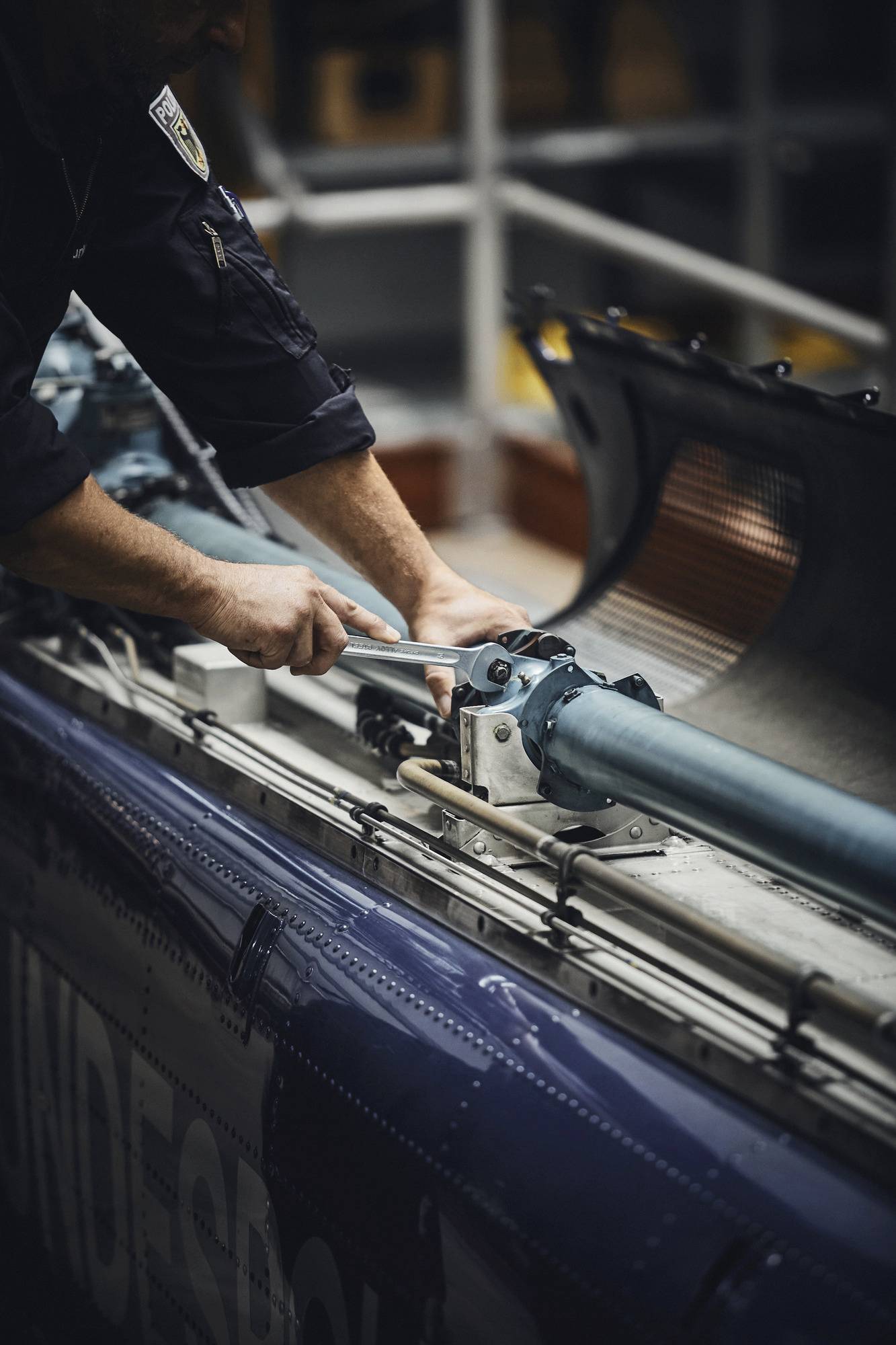 A person in uniform uses a wrench to adjust a component on machinery in a workshop setting, suggesting maintenance work.
