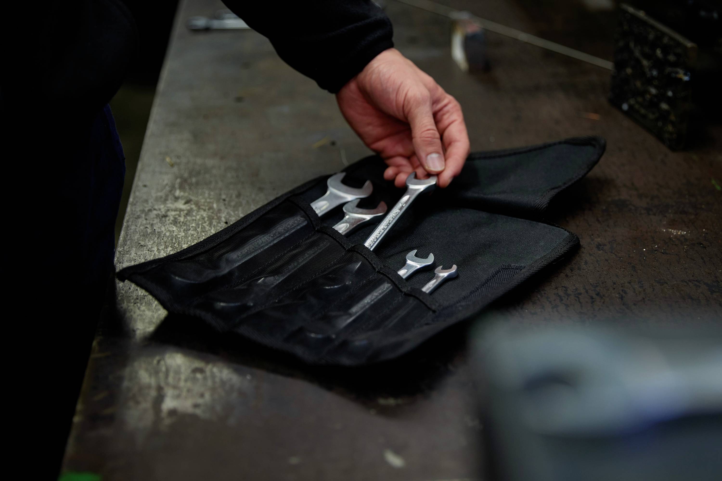 A person picks up a spanner from an open toolbag on a workbench.