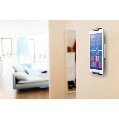 A tablet mounted on the wall controls smart home functions in a modern living room. Blurred furniture is visible in the background.