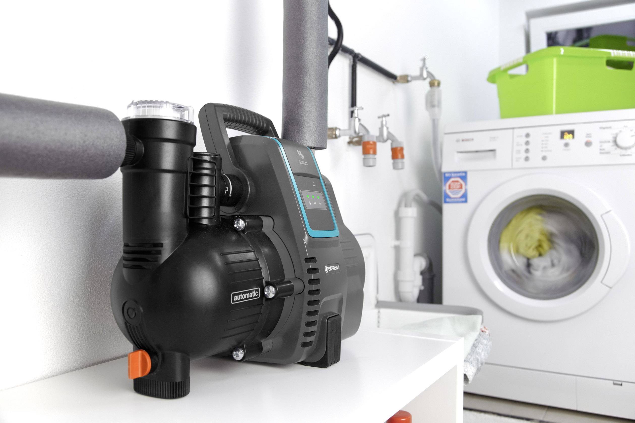 A water pump is standing on a shelf in front of a running washing machine in a utility room.