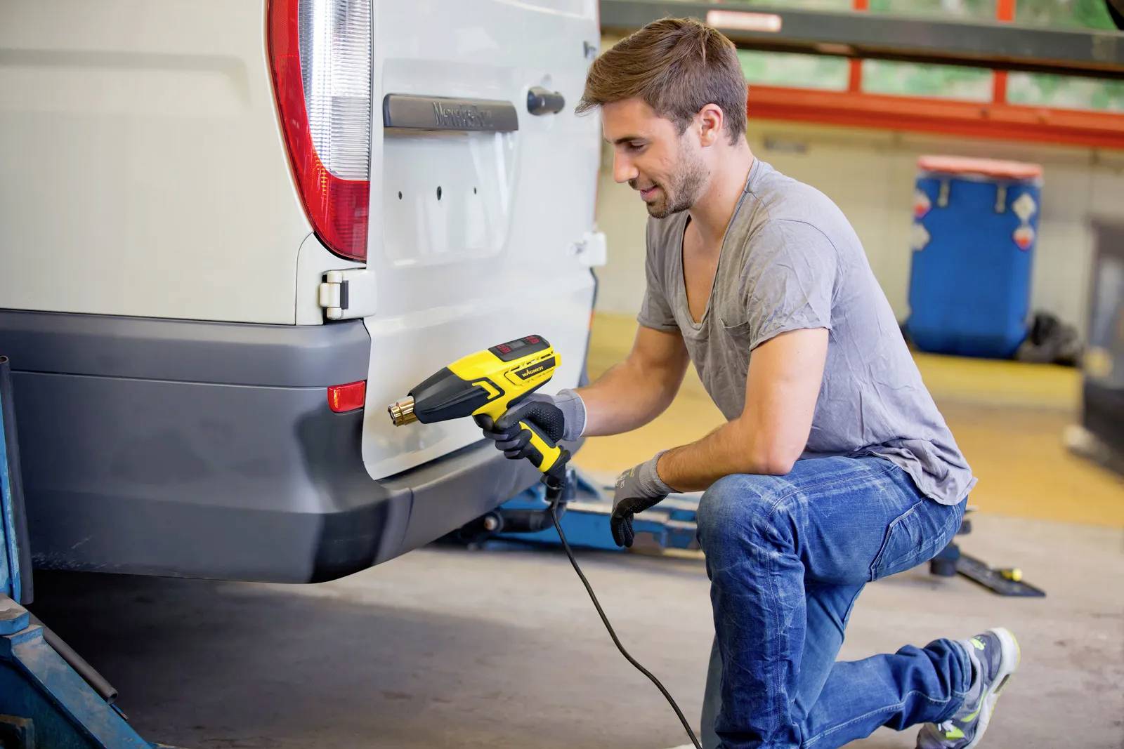 A man is kneeling beside a white delivery van and using a heat gun to apply a film to the rear of the vehicle.