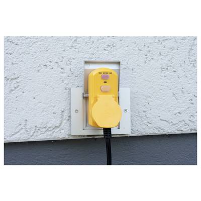 Yellow outdoor electrical outlet cover mounted on a wall, with a power cord plugged in and hanging down.