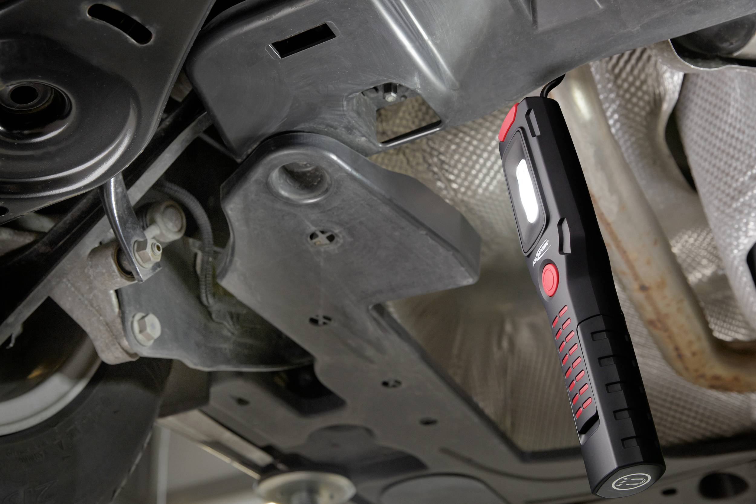 A LED lamp is illuminating under a vehicle, lighting up the engine compartment for maintenance work.