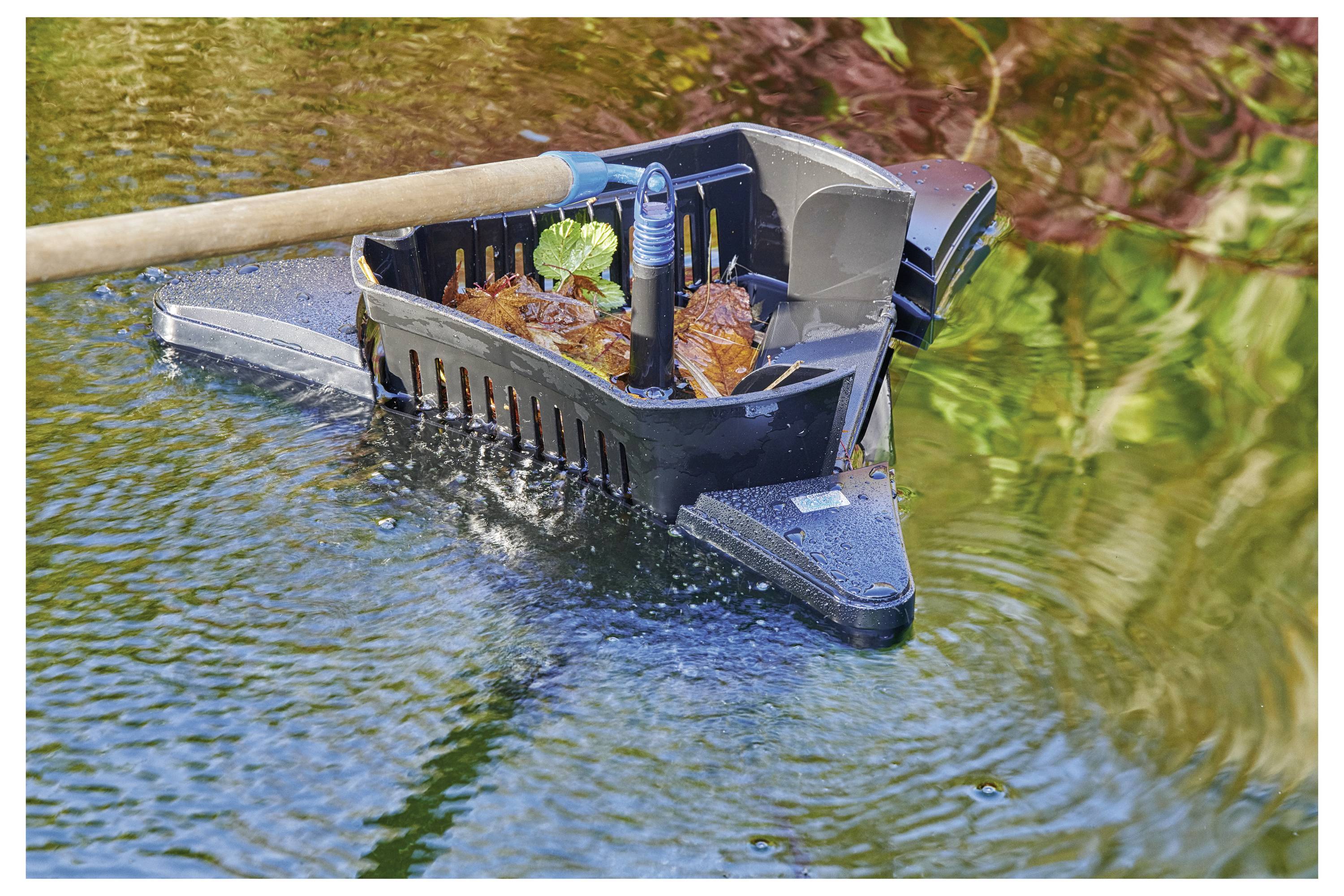 A long-handled skimmer collects fallen leaves and debris from a garden pond, showing reflection of surrounding greenery in the water.