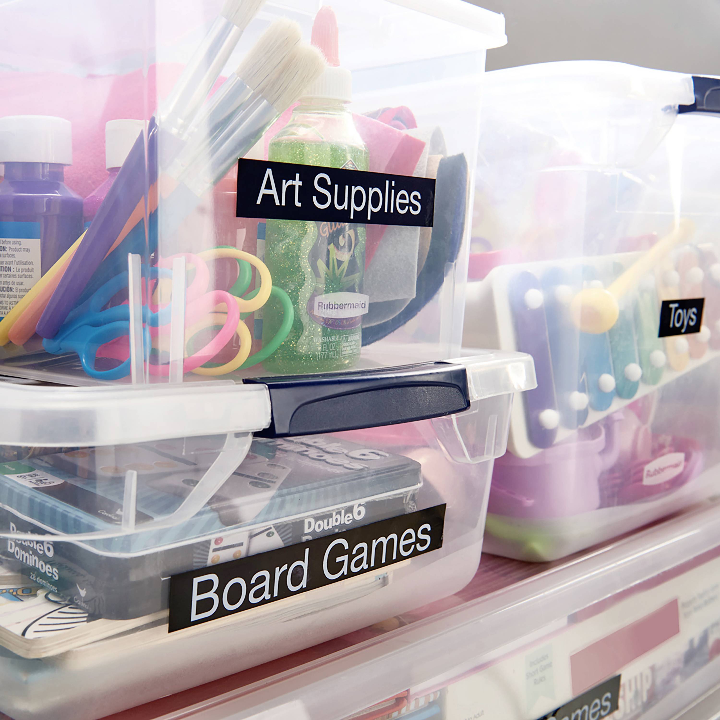 Art supplies, board games and toys in labelled plastic boxes for organised storage. Brushes and paints visible.