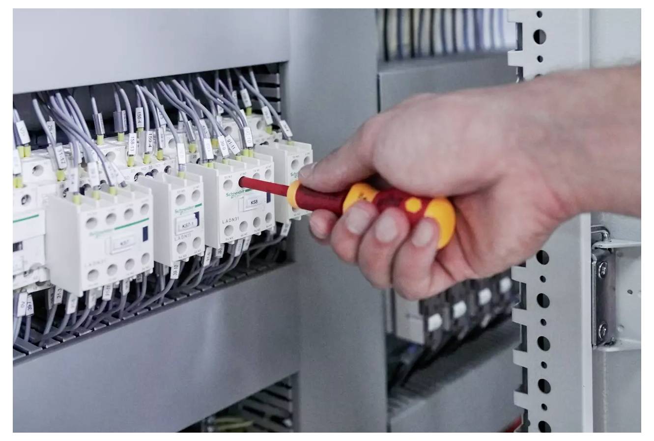 A person uses a screwdriver to adjust wiring in an electrical panel, ensuring proper connection and function of the components.