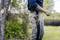 A man is standing in the garden, with a knife at his side, ready for gardening work. The background shows trees and lawn.