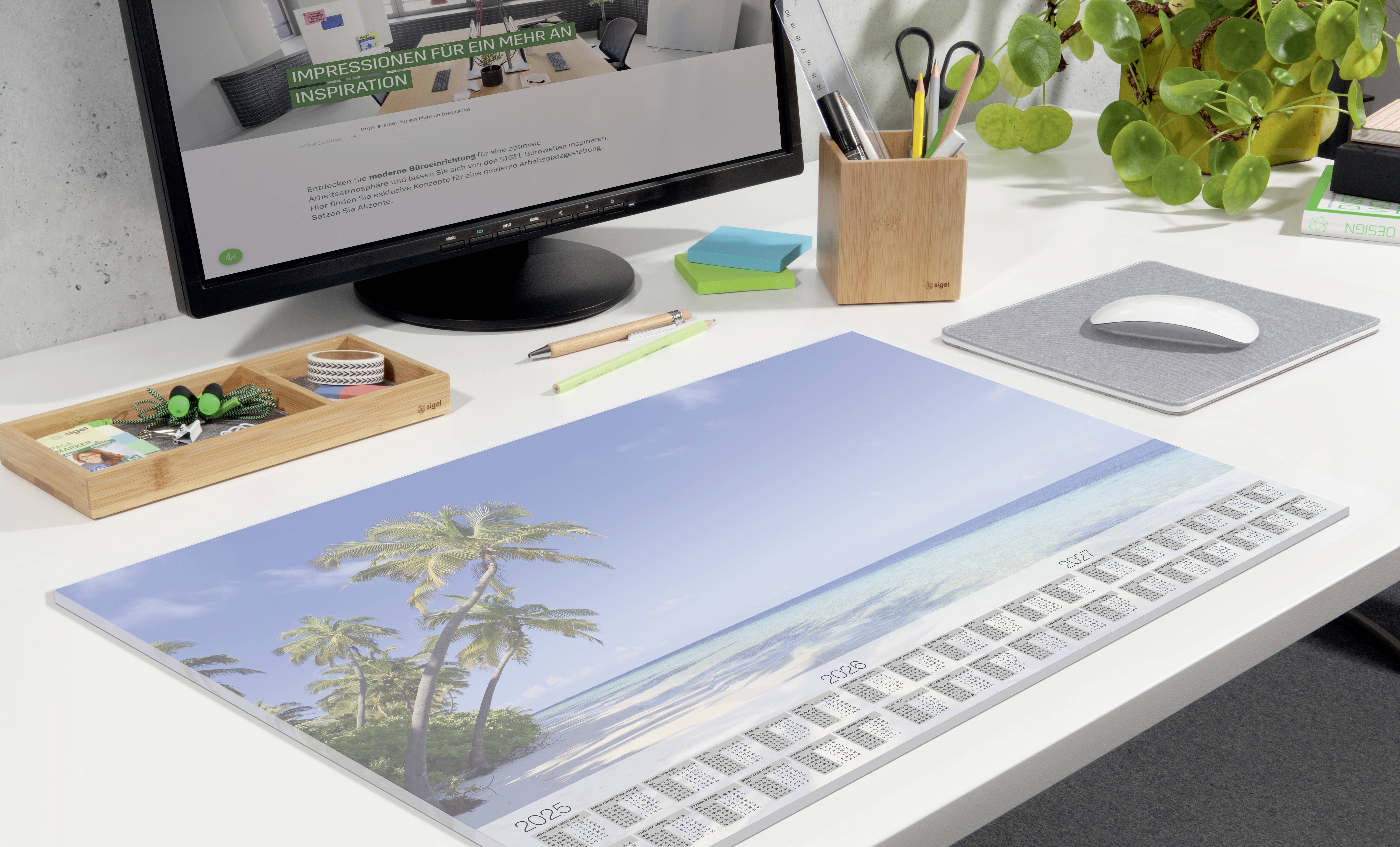 A desk with a computer monitor displaying a webpage. A calendar sheet with a beach scene is lying on the table.