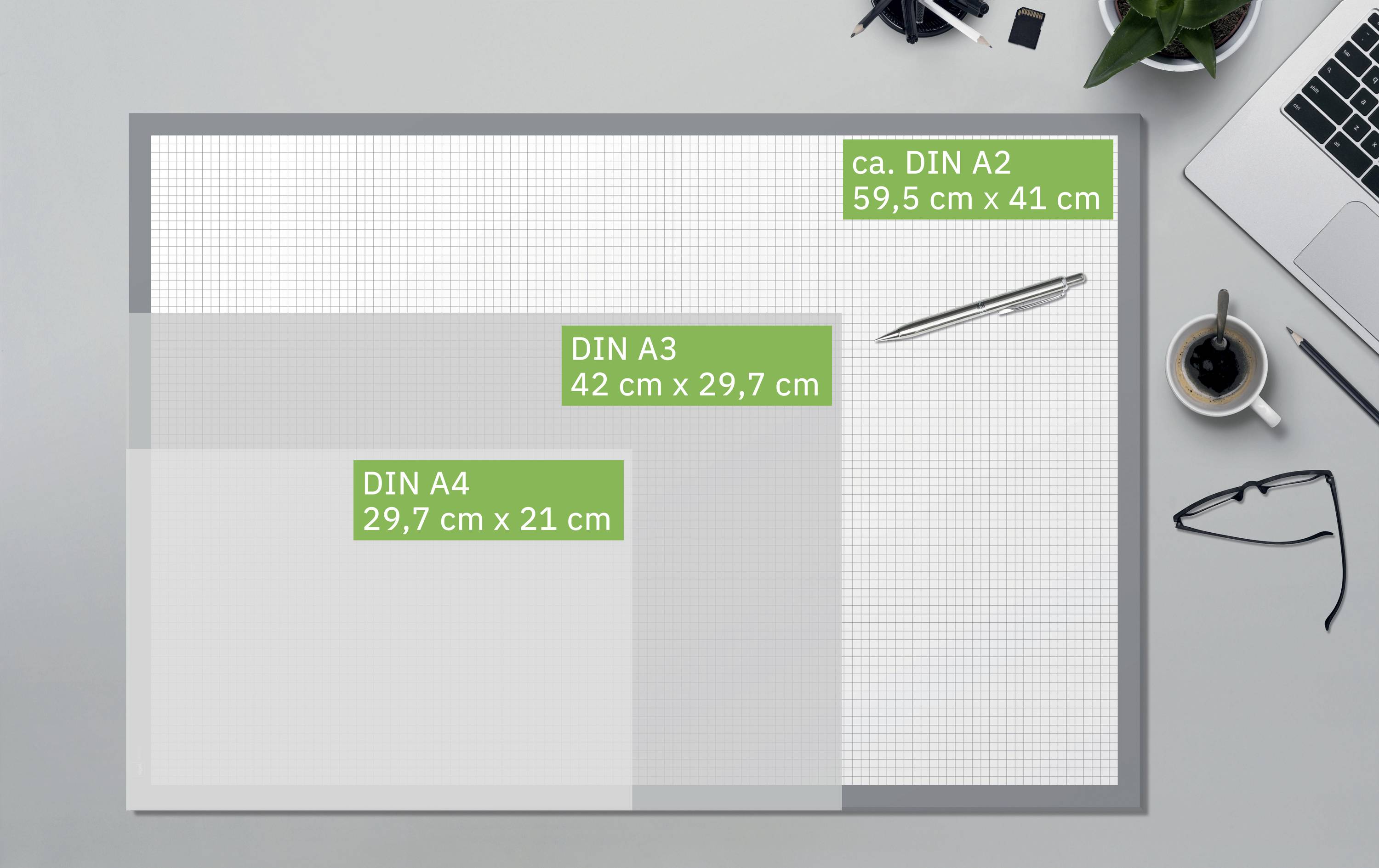'Comparison of paper sizes: DIN A2, 59.5 x 41 cm; DIN A3, 42 x 29.7 cm; DIN A4, 29.7 x 21 cm. Laptop, glasses and plant complement the image.'