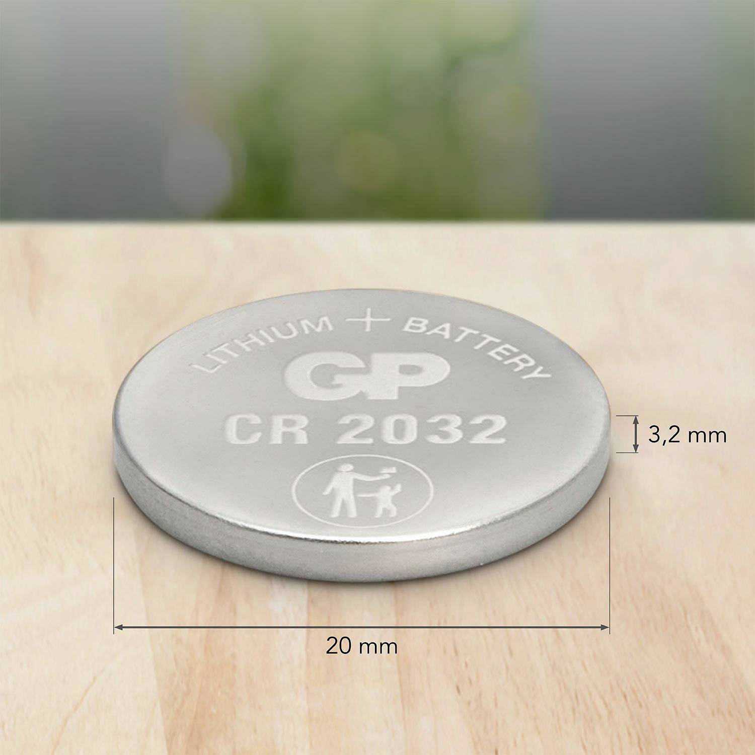 Lithium button cell with 'CR 2032' inscription, 20 mm in diameter, 3.2 mm thick. Shown on a wooden table.