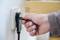A hand pulls a plug from a wall socket beneath a wooden table.