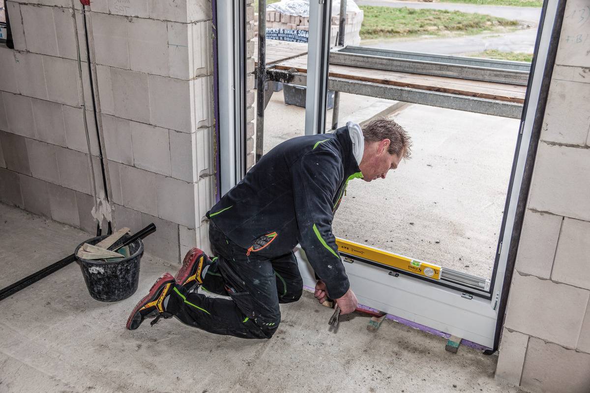 A person is installing a glass door in a building. A worker is kneeling on the floor and using a tool to secure the door.