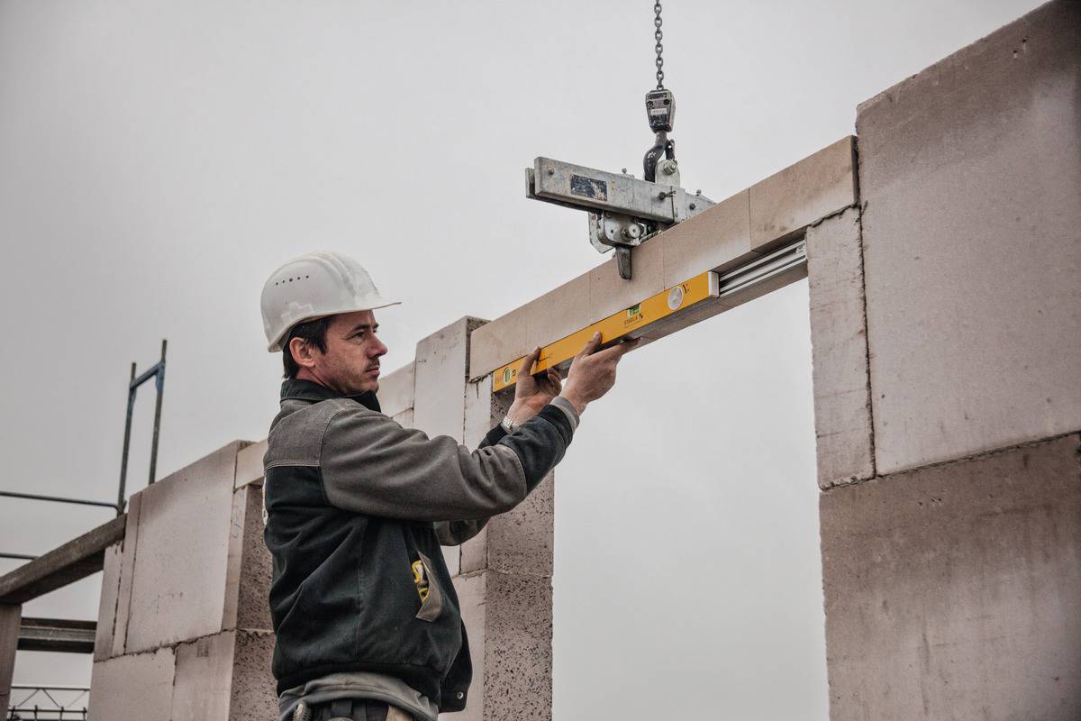 A construction worker is levelling a concrete slab on a building using a spirit level. A crane can be seen in the background.