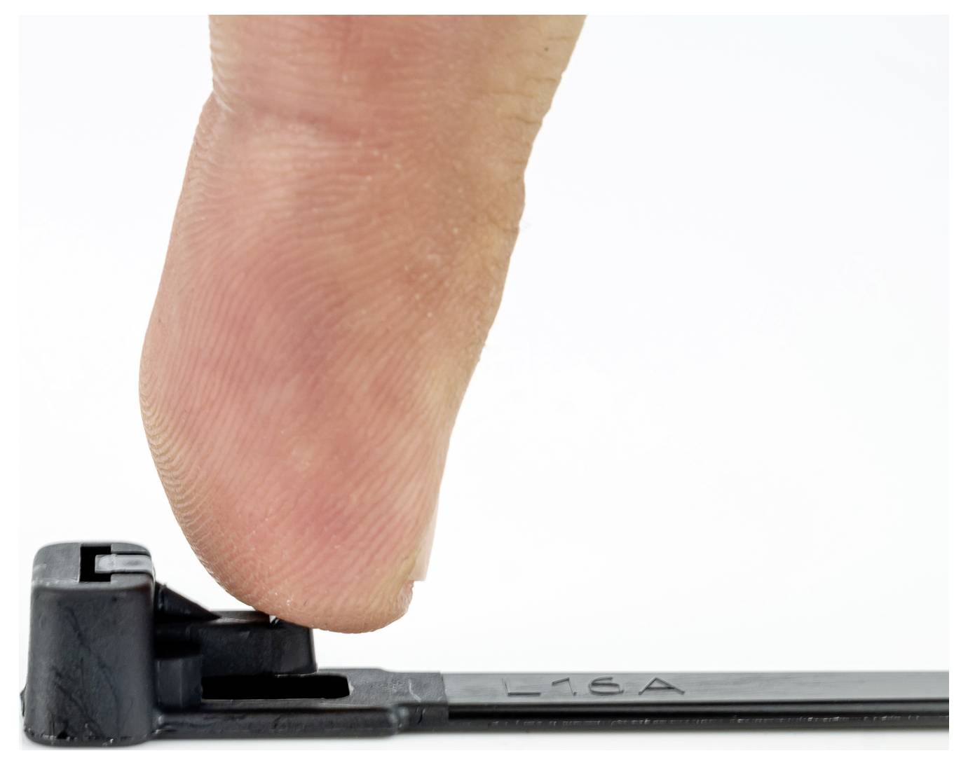 A finger pressing a black cable tie latch against a white background.