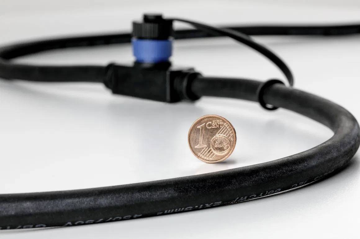 A copper penny stands upright next to a black cable with a blue connector. Focus on size comparison between the penny and the cable.
