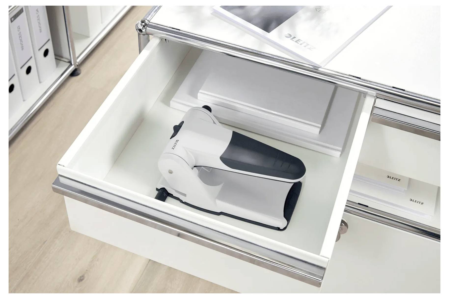 An open drawer displaying a white electrical device on top of a stack of papers. The drawer is part of a metal and wood cabinet.