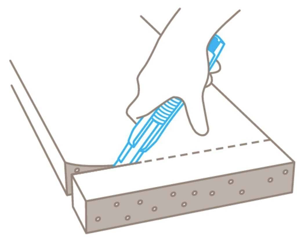 A hand cuts along a dotted line through a rectangular foam board using a blue knife.